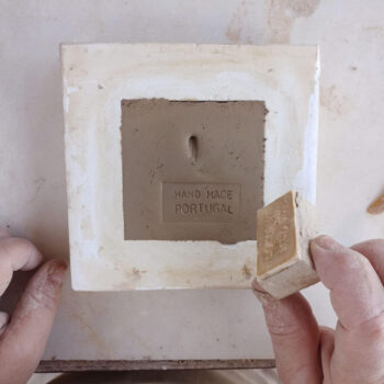 Mãos a fazer um azulejo e a carimbar a frase "Made in Portugal"