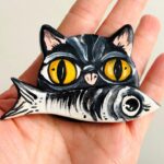 iman de gato preto e olhos laranja com sardinha na boca pintado á mão