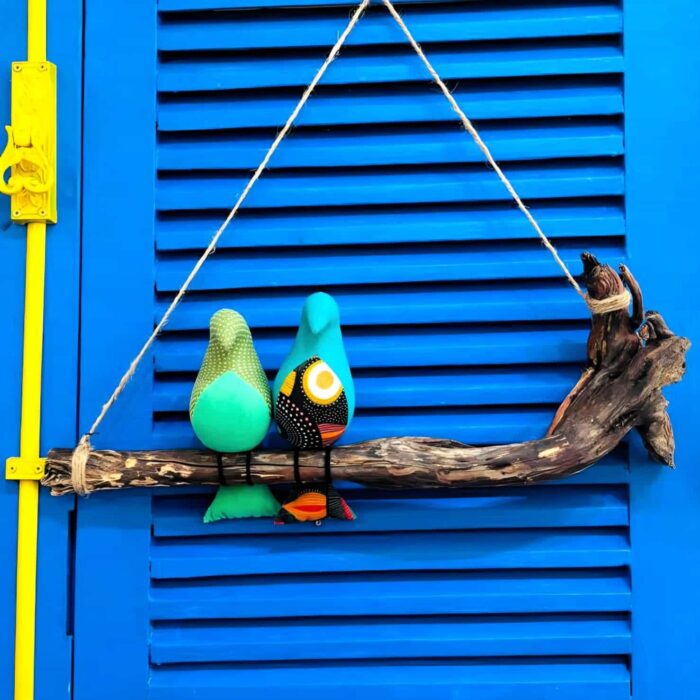 2 passarinhos de tecido azul claro, pousados num galho de madeira