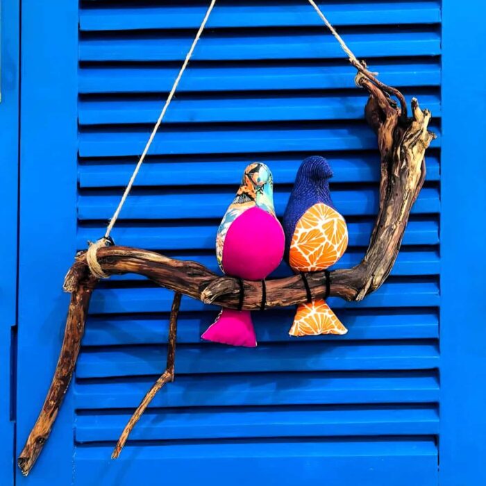 2 passarinhos de tecido lilas e azul. pousados num galho de madeira