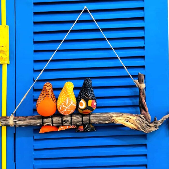 3 passarinhos de tecido amarelo, laranja e preto, pousados num galho de madeira