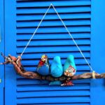 3 passarinhos de tecido azul pousados num galho de madeira