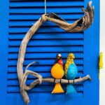 2 passarinhos coloridos de tecido amarelo e azul pousados num galho de madeira