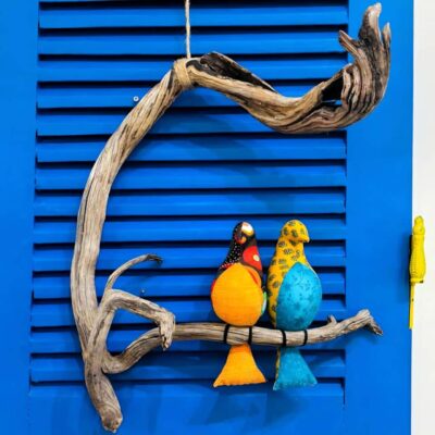 2 passarinhos coloridos de tecido amarelo e azul pousados num galho de madeira