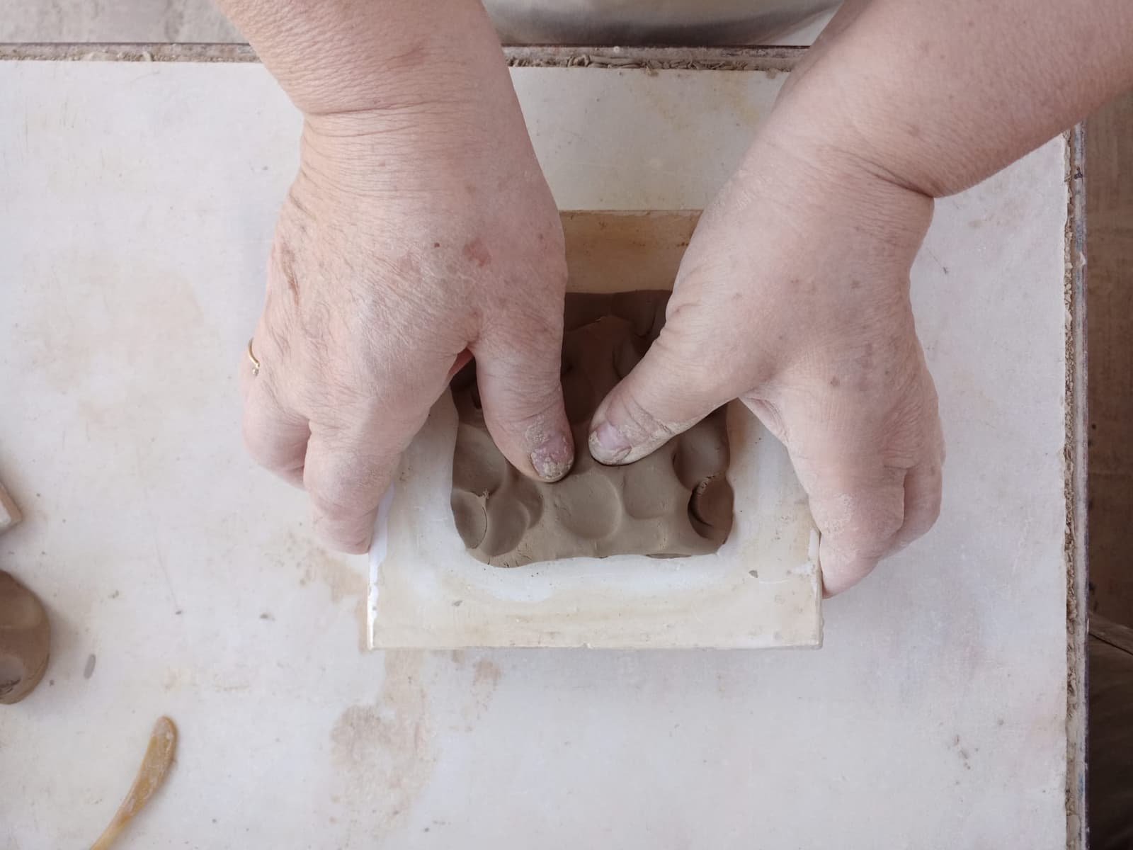 mãos de um artesão a moldarem barro num molde de azulejo