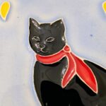 azulejo em relevo de gato preto com fundo azul e um lenço vermelho ao pescoço