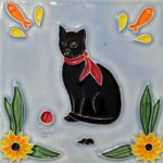 azulejo em relevo de gato preto de lenço vermelho ao pescoço, num fundo azul um ratinho preto, uma bola vermelha e flores