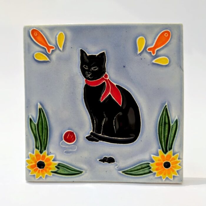 azulejo em relevo de gato preto de lenço vermelho ao pescoço, num fundo azul um ratinho uma bola vermelha e flores