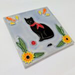 foto de perfil de azulejo em relevo de gato preto de lenço vermelho ao pescoço, num fundo azul um ratinho uma bola vermelha e flores