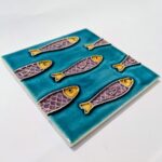 foto de perfil de azulejo português em relevo com varias sardinhas roxas e amarelas, num fundo azul