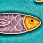 pormenor de azulejo português em relevo com varias sardinhas roxas e amarelas, num fundo azul